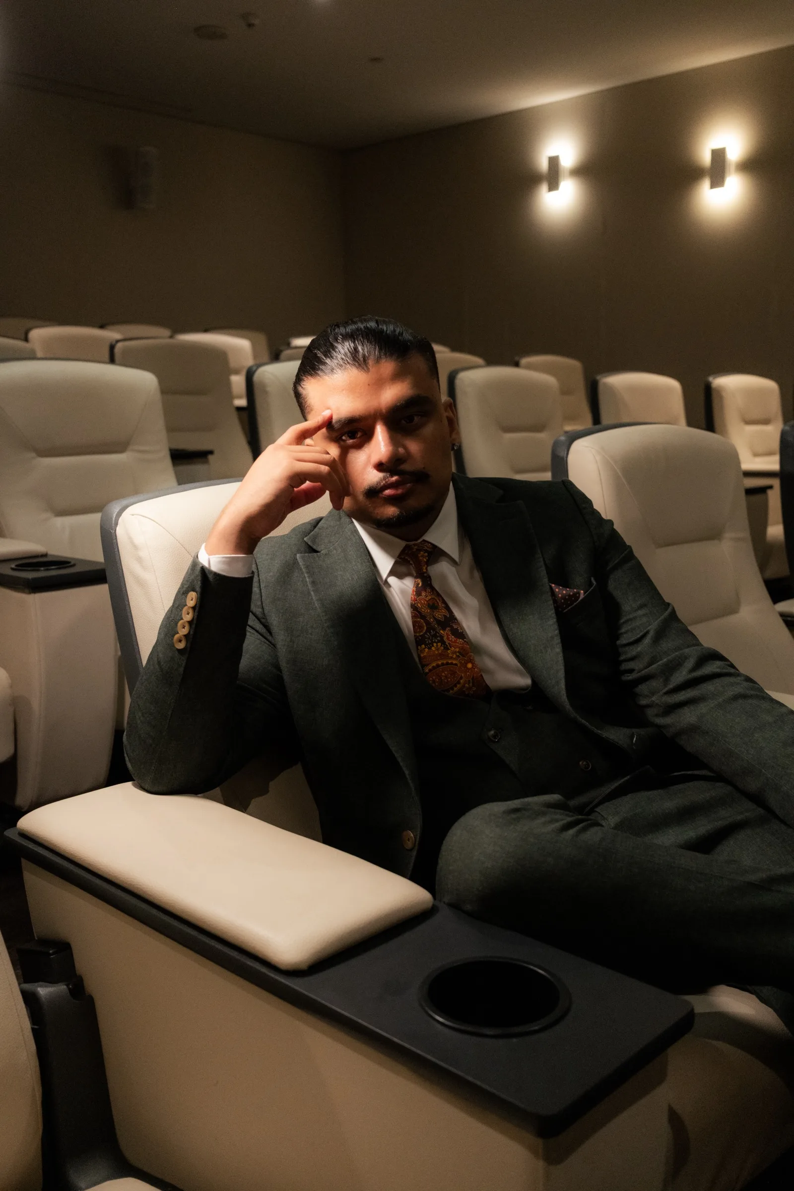 Savio Joseph seated in the Room 56 space at Hotel X Toronto, rows of seats behind him.